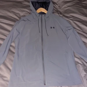 Grå vindjacka från Under Armour - Säljer en grå vindjacka från Under Armour med dragkedja och huva. Jackan har långa ärmar och är perfekt för blåsiga dagar. Den är tillverkad i ett syntetmaterial som skyddar mot väder och vind. Väldigt bra skick 8,5/10. Storlek S. Passar folk mellan 175-190 sitter riktigt bra på mig som är 185. Nypris 949 som ni ser på sista bilden, kunde inte få med hela bilden men kan visa om du hör av dig. Mitt pris 549kr. Pris kan diskuteras vid snabb affär. Hör av er vid funderingar