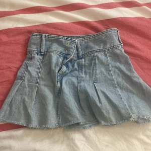 Gullig ljusblå jeanskjol - Gullig ljusblå jeanskjol med rå kant och medel midja. Kjolen har en kort längd och klassisk femficksdesign. Perfekt för en avslappnad stil.