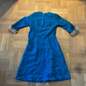Blå klänning med pälsdetaljer från Charlotta Modeller - Säljer en elegant blå klänning från Charlotta Modeller med trekvartsärmar och pälsdetaljer vid ärmsluten. Klänningen har en dragkedja i ryggen och är perfekt för en stilfull look. Passar bra för höst och vinter.            Kläning från 1800-talet typ. Killarna kommer springa efter er med den här på er👍👍