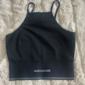 Svart linnetopp från Calvin Klein Jeans - Säljer en stilren svart linnetopp från Calvin Klein Jeans med smala axelband och logga framtill. Perfekt för en casual look eller att matcha med dina favoritjeans.