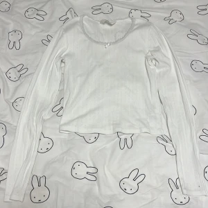 Vit långärmad topp från H&M - Säljer en söt vit långärmad topp från H&M. Toppen har en fin spetsdetalj runt halsringningen och en liten rosett framtill. Den är ungefär magtröja och ser genomskinlig så ni bara vet💗 