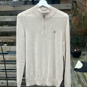 Beige merinoulltröja från Morris - Säljer en stilren beige tröja från Morris i 100% merinoull. Tröjan har en dragkedja vid halsen och ett diskret broderat emblem på bröstet. Perfekt för kyligare dagar med sin mjuka och bekväma passform.     Inga fläkar eller hål eller annat dåligt. Skirv vid frågor. Priset ej hugget i sten. Köptes för 1199.             