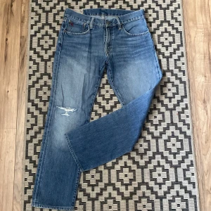 Blå jeans från Polo Ralph Lauren - Snygga blå jeans från Polo Ralph Lauren med en klassisk femficksdesign. De har en liten röd broderad logga på myntfickan och en sliten detalj på ena benet. Perfekta för en avslappnad stil. Nypris 2300