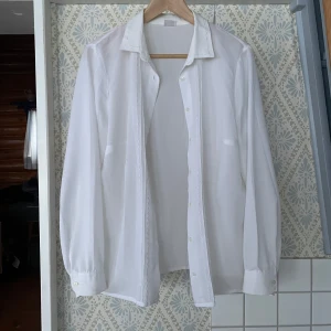 Vit skjorta med broderade detaljer - Vit skjorta med subtila broderade detaljer längs knappraden. Lite transparent. Storlek 51 enligt märke, M/L skulle jag säga 