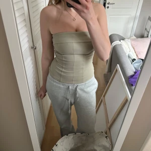 Beige tubtopp från Divided - Säljer en stilren beige tubtopp från Divided. Perfekt för att skapa en chic look. Toppen är axelbandslös och har en tight passform som framhäver figuren. Passar utmärkt till både jeans och kjol. Hör av dig vid intresse!