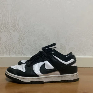 Svartvita Nike Dunk sneakers - Snygga svartvita Nike Dunk sneakers med klassisk design. Skorna har en låg profil och är tillverkade i skinn med snörning framtill. Perfekta för en stilren look. Lite använda.