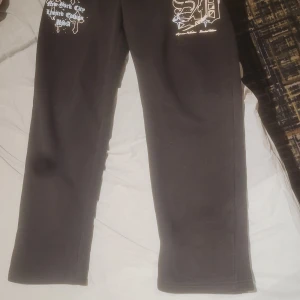 Svarta byxor från Supply & Demand - Svarta byxor från Supply & Demand med tryck på benen. De har en avslappnad passform och är perfekta för en casual look. Byxorna har elastisk midja för extra komfort.