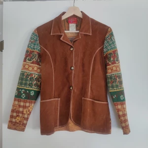 Brun mockajacka från Kenzo - Unik brun mockajacka från Kenzo med färgglada mönstrade ärmar i grönt, rött och gult. Jackan har knappar framtill och två fickor. Perfekt för dig som vill sticka ut med en stilfull och annorlunda look.