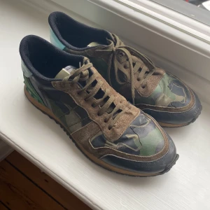 Valentino Rockrunner i camouflage - Snygga Valentino Rockrunner sneakers i ett coolt camouflage-mönster. Skorna har snörning och är tillverkade i en mix av mocka och syntetmaterial. De har en unik design med gröna detaljer på hälen.