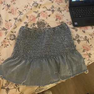 tubbtopp i jeans material - Tubbtopp med volang och smockad överdel. Storlek M men eftersom det är stretchigt material funkar den för L också. Inprincip aldrig använd!