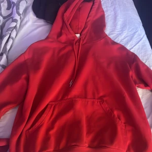 Röd hoodie - Säljer en snygg röd hoodie med känguruficka och justerbar huva. Perfekt för en avslappnad stil och passar bra till både jeans och joggers. Den har en klassisk design med ribbade muddar vid ärmslut och nederkant.