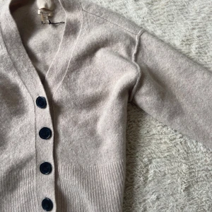 Beige kofta från H&M - Mysig beige kofta från H&M med knappar framtill. Perfekt för sommarkvällar och väldigt mjuk. Koftan har en v-ringad design och långa ärmar.