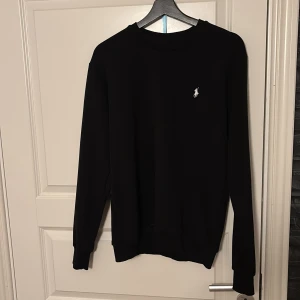 Svart tröja från Ralph Lauren - Säljer en stilren svart tröja från Ralph Lauren med deras ikoniska logga broderad i vitt på bröstet. Tröjan har långa ärmar och en klassisk rund halsringning. Helt oanvänd med det sagt inga defekter. Prise kan diskuteras