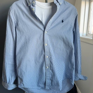 Blå och vit randig skjorta från Ralph Lauren - Snygg blå och vit randig skjorta från Ralph Lauren med klassisk krage och knappar framtill. Perfekt för en stilren look! Kom dm för frågor.