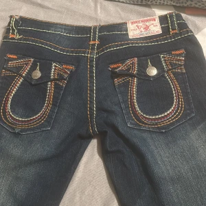 Blåa jeans från True Religion - Snygga blå jeans från True Religion med unika broderade bakfickor och kontrastsömmar. Perfekta för en stilren look med en touch av attityd.