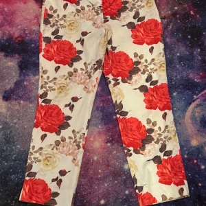 Blommiga byxor med röda rosor - Snygga byxor med ett färgglatt blommönster i rött och beige på en vit bakgrund. 