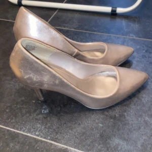 Guldiga pumps med spetsig tå - Snygga guldiga pumps med spetsig tå och klack. Perfekta för att lägga till lite glamour till din outfit. De har en elegant design som passar bra till festliga tillfällen. Lite defekter