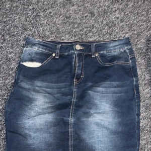 Jeanskjol från KappAhl - Snygg jeanskjol från KappAhl i en klassisk blå tvätt. Kjolen har en normal passform med fickor både fram och bak samt en knapp och dragkedja framtill. Perfekt för en avslappnad stil.