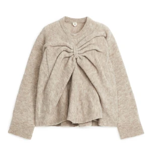 Beige stickad tröja med knytning - Säljer en mysig beige stickad tröja med unik knytning framtill. Tröjan har långa ärmar och en avslappnad passform, perfekt för kyliga dagar. Den är både stilren och bekväm, ett måste i garderoben!