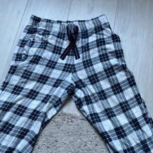 Rutig byxa från Kappahl - Säljer ett par bekväma rutiga byxor från Kappahl i storlek XS. Byxorna har ett elastiskt midjeband med snörning och är perfekta för en avslappnad stil. De har en klassisk svart och vit färgkombination.