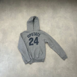 Grå hoodie med tryck - Säljer en grå hoodie med texten 'UPSTATE 24' tryckt på framsidan. Tröjan har en klassisk design med huva och långa ärmar. Perfekt för en avslappnad stil.