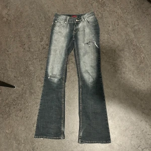 Snygga Blå bootcut jeans med slitningar! - Snygga blå bootcut jeans med coola slitningar på framsidan. Aldrig använda men köpta här på Plick. Tyvärr för stora för mig!  Skriv vid frågor eller funderingar💗