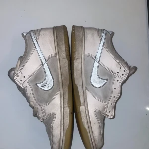 Nike Dunk i beige och vit - Säljer ett par Nike Dunk sneakers i beige och vit med klassisk snörning. Skorna har en stilren design med den ikoniska Nike-loggan i silver på sidan. Perfekta för en avslappnad stil.( PRIS KAN DISKUTERAS)