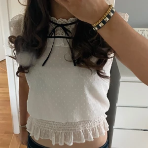 Vit blus med spets och volangdetaljer - Charmig vit blus med spetsdetaljer och volang vid ärmslut och nederkant. Blusen har en söt rosett vid halsen som går att ta bort och ett diskret prickigt mönster. Perfekt för en somrig look! Storlek 146/152 men passar mig som oftast bär Xs/S, bilderna är mina egna! Pris kan diskuteras