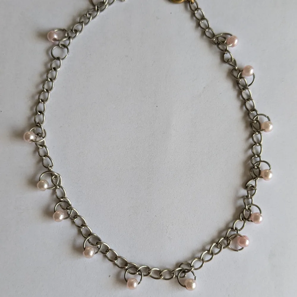 Elegant halsband med silverfärgad kedja och små vita pärlor jämnt fördelade längs kedjan. Perfekt för att ge en stilren touch till din outfit.. Asusteet.