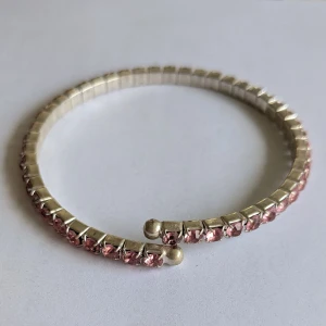 Silverfärgat armband med rosa stenar - Elegant armband i silverfärg med gnistrande rosa stenar. Perfekt för att ge en touch av glamour till din outfit. Armbandet har en flexibel design som gör det enkelt att ta på och av.