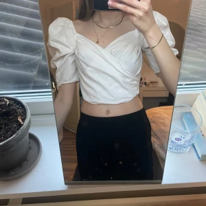 Vit omlott blus - Säljer en stilren vit omlott blus med puffiga korta ärmar. Blusen har en croppad passform och en elegant v-ringning. Perfekt för en trendig look!