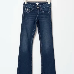 Mörkblå bootcut jeans - Snygga mörkblå bootcut jeans med kontrasterande vita sömmar och fickdetaljer. Jeansen har en klassisk femficksdesign och en knappgylf. Perfekta för en avslappnad stil.