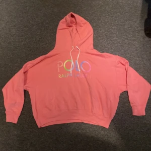 Rosa hoodie från Ralph Lauren - Säljer en snygg rosa hoodie från Ralph Lauren med färgglatt tryck på framsidan. Den har en bekväm passform och en klassisk huva med dragsko. Perfekt för en avslappnad stil.