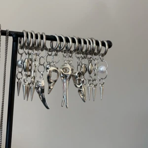 Silver örhängen i rostfritt stål  - Unika örhängen med olika silverdetaljer som fågelskallar, nitar och pärlor, för en extra touch. Perfekt för att ge din stil en edgy känsla. Säljes styckvis!
