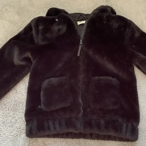 Svart pälsjacka från H&M - Säljer en snygg svart pälsjacka från H&M. Jackan har en dragkedja framtill och två fickor. Perfekt för att hålla sig varm och stilren under kyliga dagar.