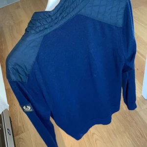 Mörkblå tröja med dragkedja från Belstaff - Säljer en stilren mörkblå tröja från Belstaff med dragkedja och quiltade axelpartier. Tröjan har långa ärmar och en normal passform. Perfekt för en avslappnad men ändå snygg look.