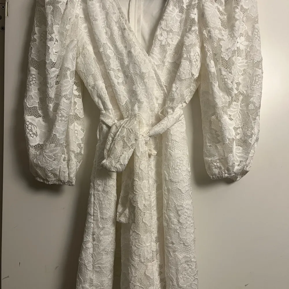 Elegant vit jumpsuit från Sisters Point i omlottmodell. Jumpsuiten har långa ärmar och ett knytband i midjan för en smickrande passform. Perfekt för speciella tillfällen.. Mekot.