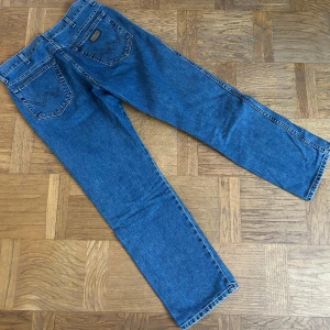 Jeans Wrangler - Snygga blå jeansbyxor med klassisk femficksdesign och broderad detalj på bakfickan. Byxorna har en rak passform och är perfekta för en avslappnad stil. De har en midwaist och är tillverkade i slitstarkt denim.