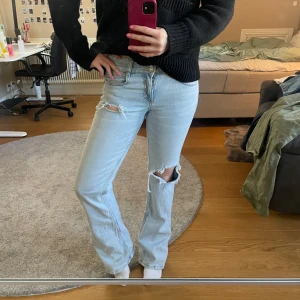 Ljusblå jeans med slitningar - Snygga ljusblå jeans med slitningar på knäna. De har en klassisk femficksdesign och två  knappar. Perfekta för en avslappnad stil.