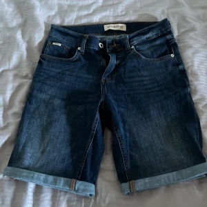Mörkblå jeansshorts från Lindbergh använda en gång  - Snygga mörkblå jeansshorts från Lindbergh med klassisk femficksdesign och uppvikta benslut. Perfekta för en avslappnad stil. De har en dragkedja och knapp framtill.