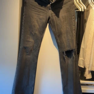 Mörkgrå jeans med hål  från Ginatricot - Snygga svarta jeans med en slitning på ena benet. De är bootcut och mid waist. Väldigt fint skick 