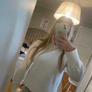Vit stickad tröja - Säljer en stilren vit stickad tröja med långa ärmar och ribbade detaljer vid ärmslut och nederkant. Perfekt för kyligare dagar och lätt att matcha med olika outfits.