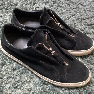 Axel Arigato skor - Snygga svarta sneakers från Axel Arigato i mocka med dragkedja framtill. Skorna har en vit sula och en stilren design som passar perfekt för en modern look. Säljer skorna för att dom inte kommer till användning. Priset är inte hugget i sten. 