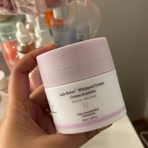 Lala Retro Whipped Cream - Lala Retro Whipped Cream från Drunk Elephant är en återfuktande ansiktskräm med en blandning av tre ceramider och afrikanska oljor. Den kommer i en stilren burk med ljusrosa lock och rymmer 50 ml. Perfekt för att ge huden en extra dos av fukt och näring.