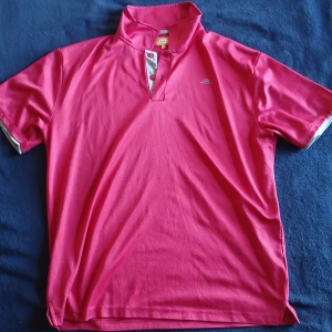 Röd kortärmad t-shirt från Nordcap - Säljer en snygg röd kortärmad t-shirt från Nordcap. T-shirten har en stilren design med en knappdetalj vid halsen och kontrasterande vita kanter. Bra till träning för de är ett tunt material och den är röd ser ut som råsa men den är röd.