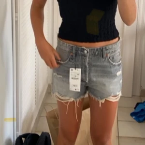 Grå jeansshorts med slitningar - Säljer ett par grå jeansshorts med coola slitningar och fransiga kanter. Shortsen har en klassisk femficksdesign och knappgylf. Perfekta för en avslappnad stil.