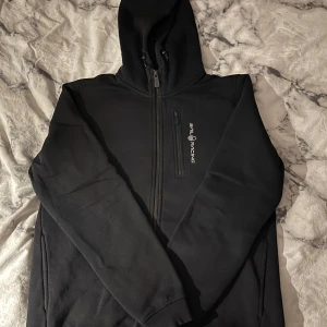 Svart hoodie från Sail Racing - Säljer en svart hoodie från Sail Racing med dragkedja och huva. Tröjan är i barnstorlek 172 men passar även dig som brukar ha XS och möjligtvis S på tröjor!