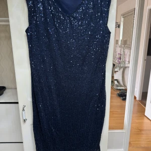 Mörkblå glittrig klänning från May - Snygg mörkblå klänning från May med glittriga paljetter över hela ytan. Klänningen har en v-ringad design och är ärmlös, perfekt för en festlig kväll. Den är både elegant och iögonfallande.