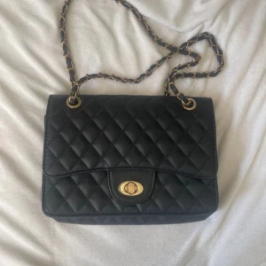 Svart quiltad axelväska - Snygg svart quiltad axelväska med guldfärgade detaljer och kedja. Väskan har en vridlåsning som har tappat lite av färgen. Skriv om man har frågor❤️