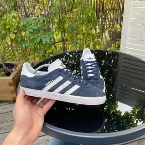 Adidas Gazelle Mörkblå - Mörkblå adidas gazelle skor i mycket bra skick, inga skador eller defekter. Perfekta skor till hösten. Hör av er vid frågor eller funderingar!! (Strl 38,5 men passar mer som 39-40)